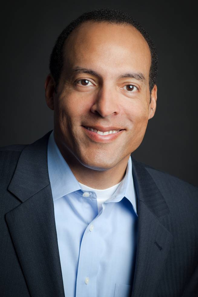 Michael Boulware Moore smiling in an open-collar portrait